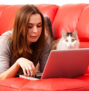 A woman on a laptop with her cat beside her